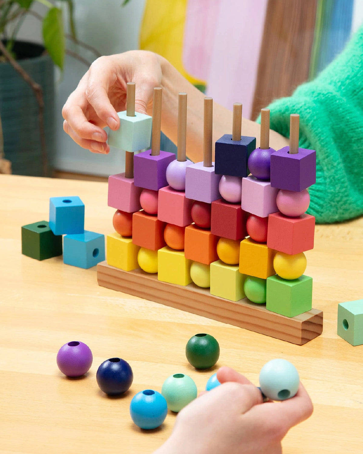 Hands dropping rainbow wooden cubes and balls onto the pegs of the Four in a Row game