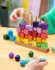 Hands dropping rainbow wooden cubes and balls onto the pegs of the Four in a Row game