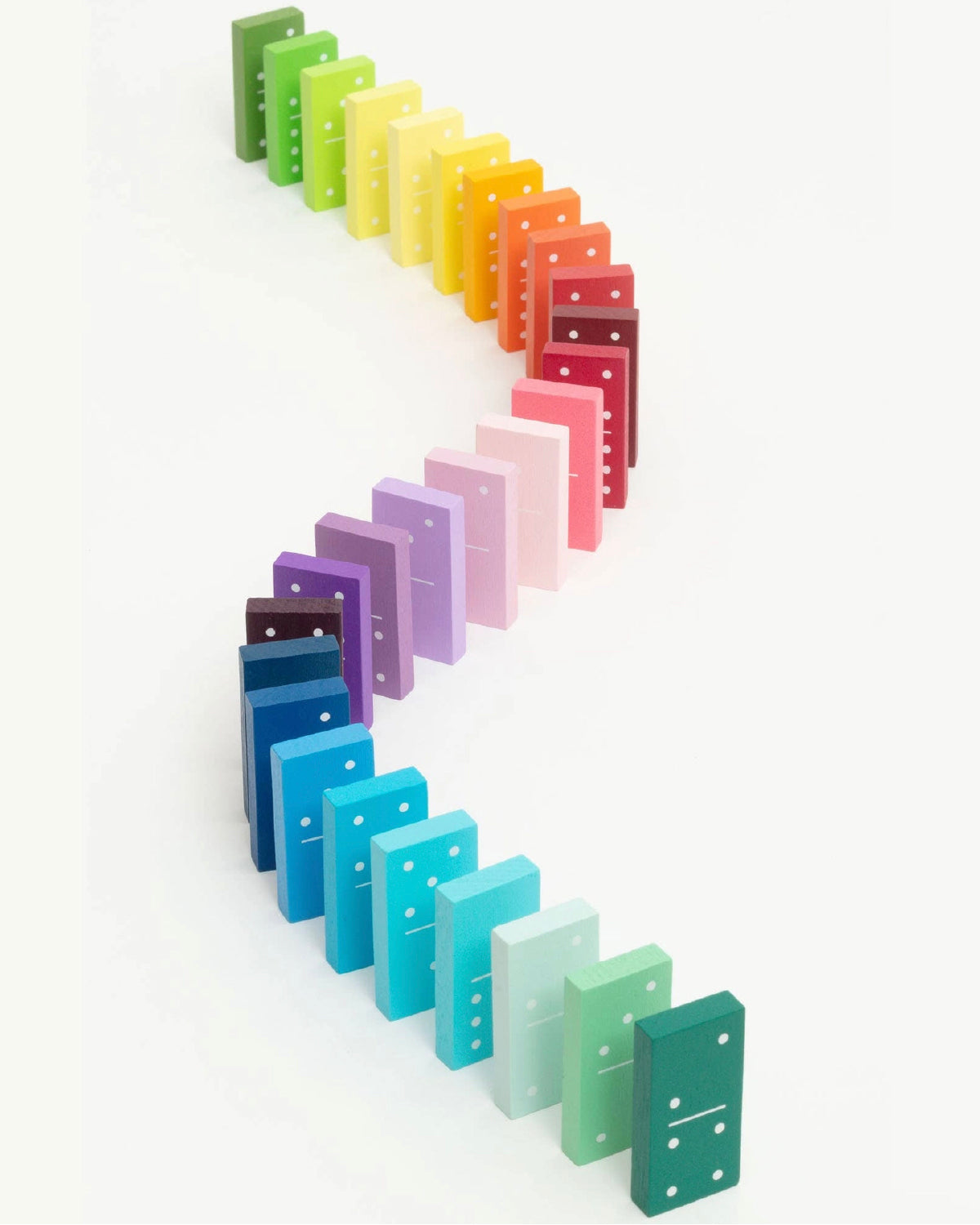 Rainbow gradient wooden dominoes standing in an S-shaped line on white