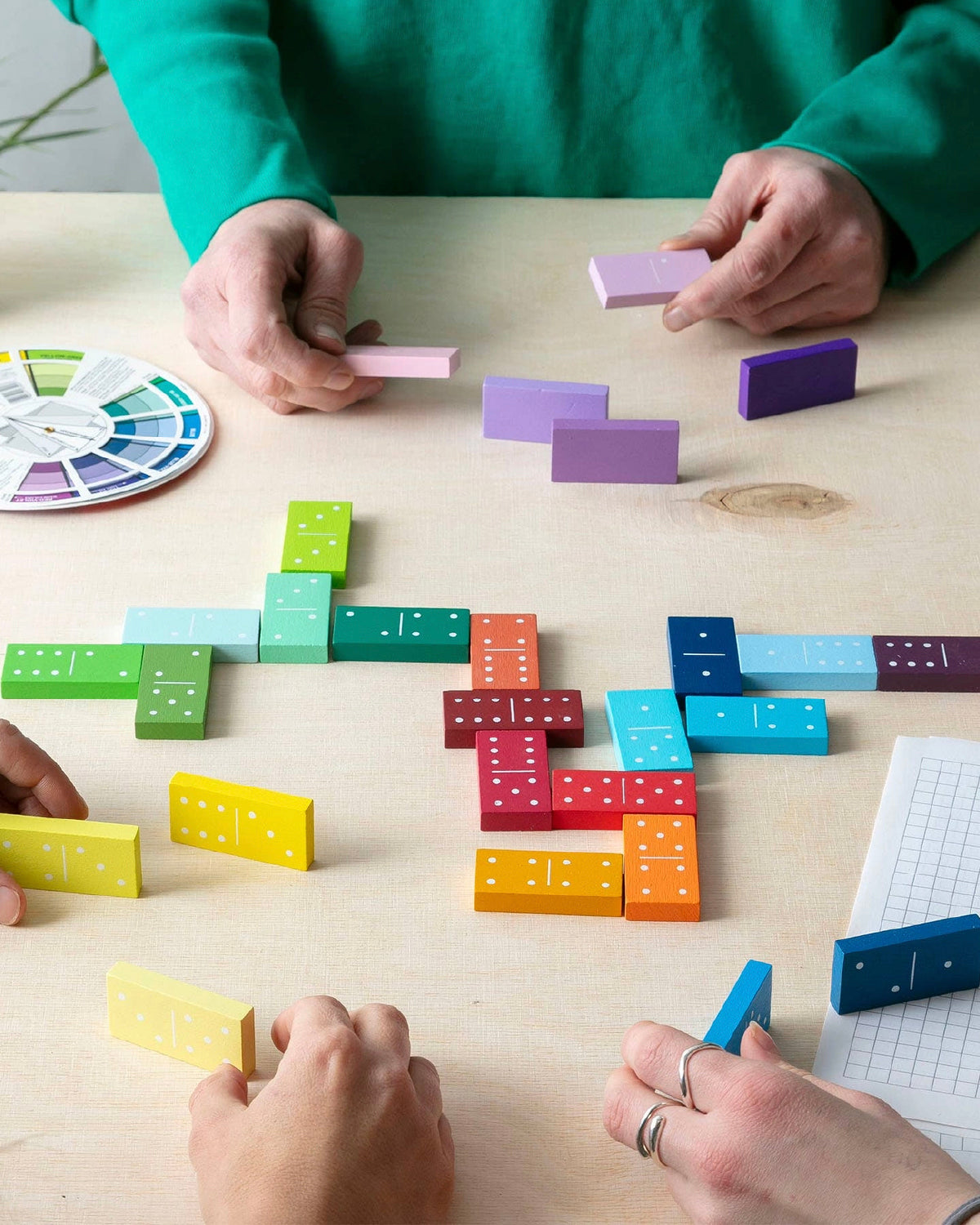 Hands playing a game of Block Design Gradient Dominoes on a light wood table
