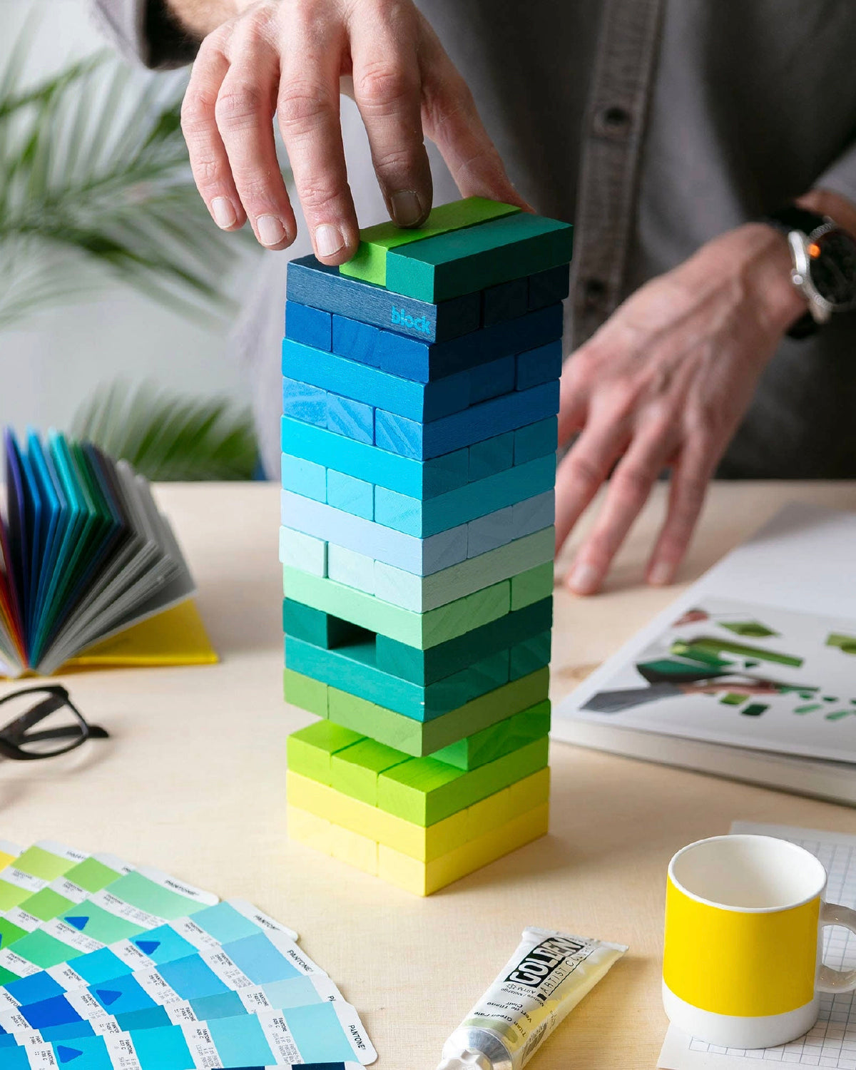 Hand placing a block on top of a Gradient Tower mid-game on a work table