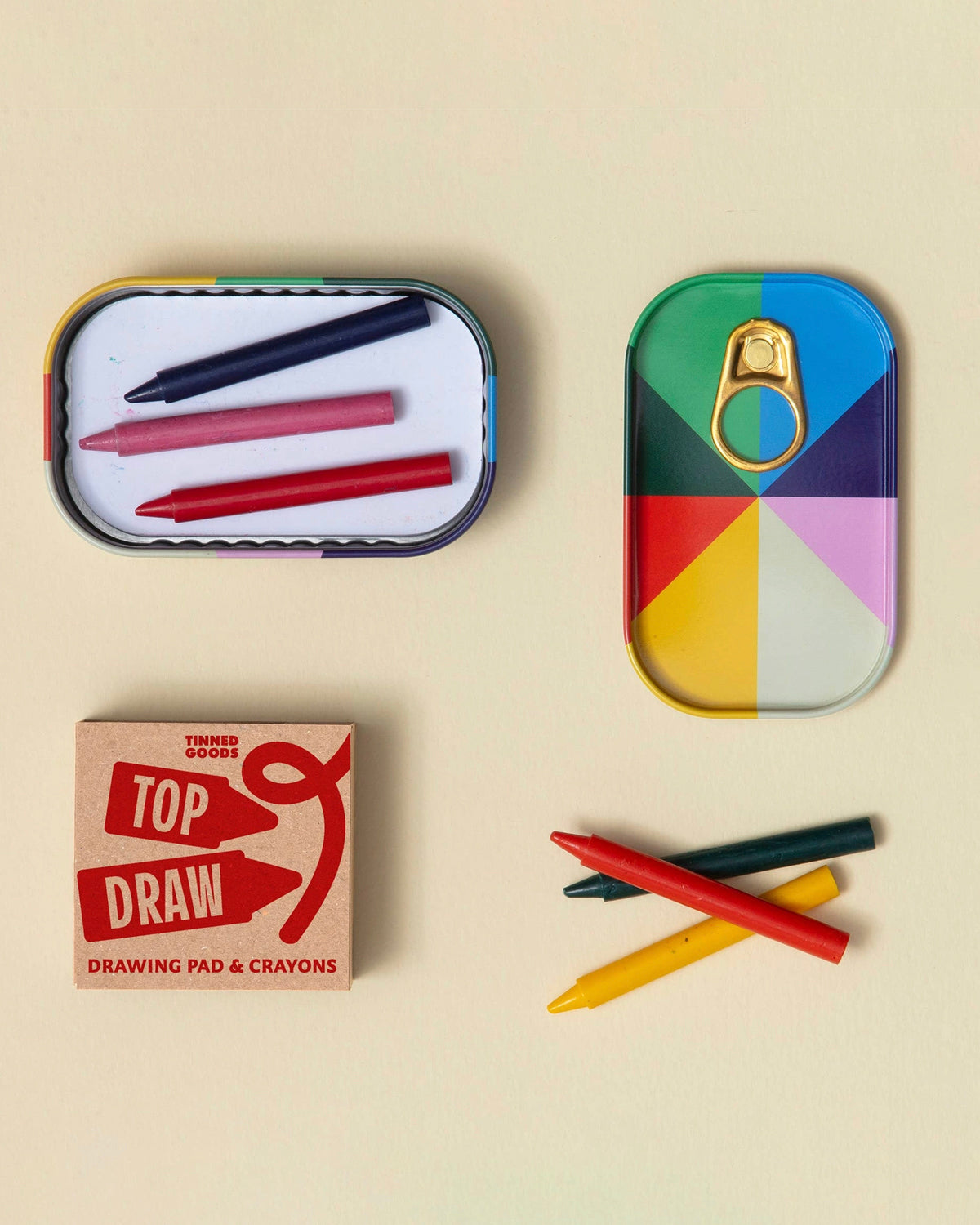 Open Block Design tin with crayons beside a colorful closed tin and its Top Draw sleeve
