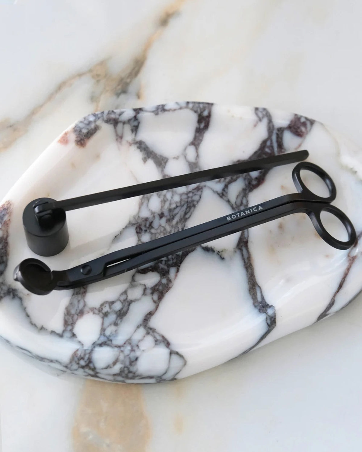 Botanica wick trimmer and bell snuffer in matte black on an oval marble tray
