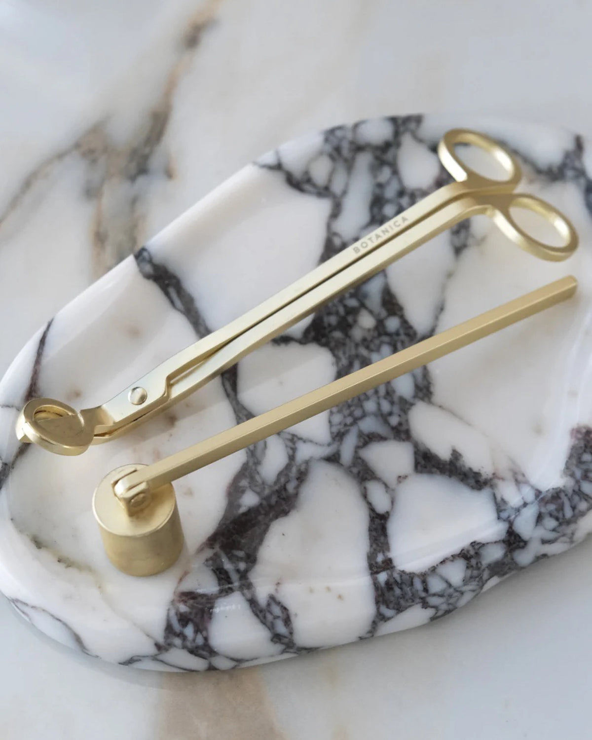 Botanica wick trimmer and bell snuffer in matte brass on an oval marble tray