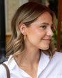 A woman with blonde-highlighted shoulder-length hair wearing a white collared shirt and a gold leaf-shaped dangle earring, shown in a close-up profile view.