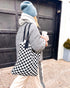 Woman in a puffer jacket walking with the Casupo black and white checkered woven tote
