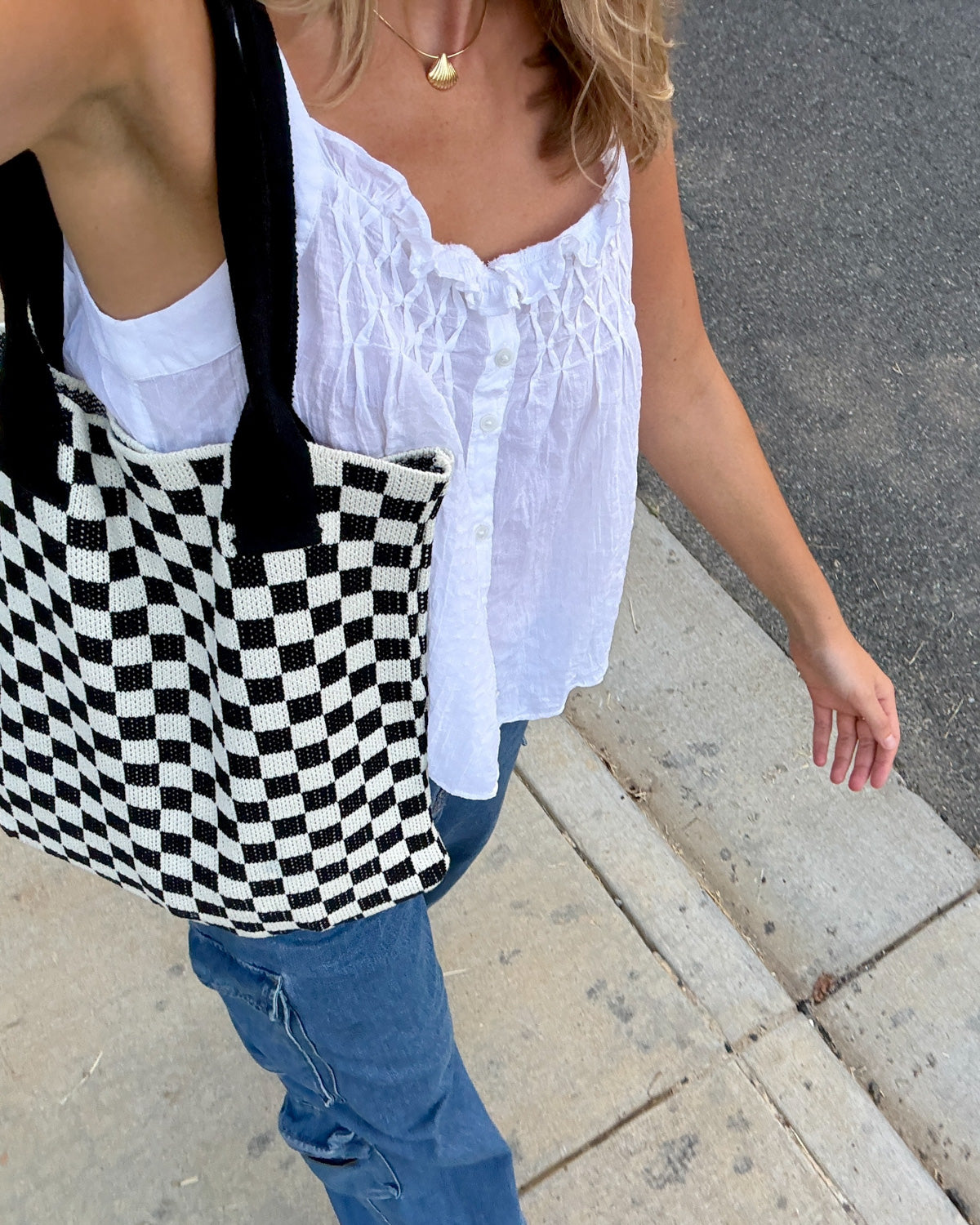 Woman walking while wearing a woven black and white checkered tote bag from Casupo paired with a white top and a pair of jeans. 