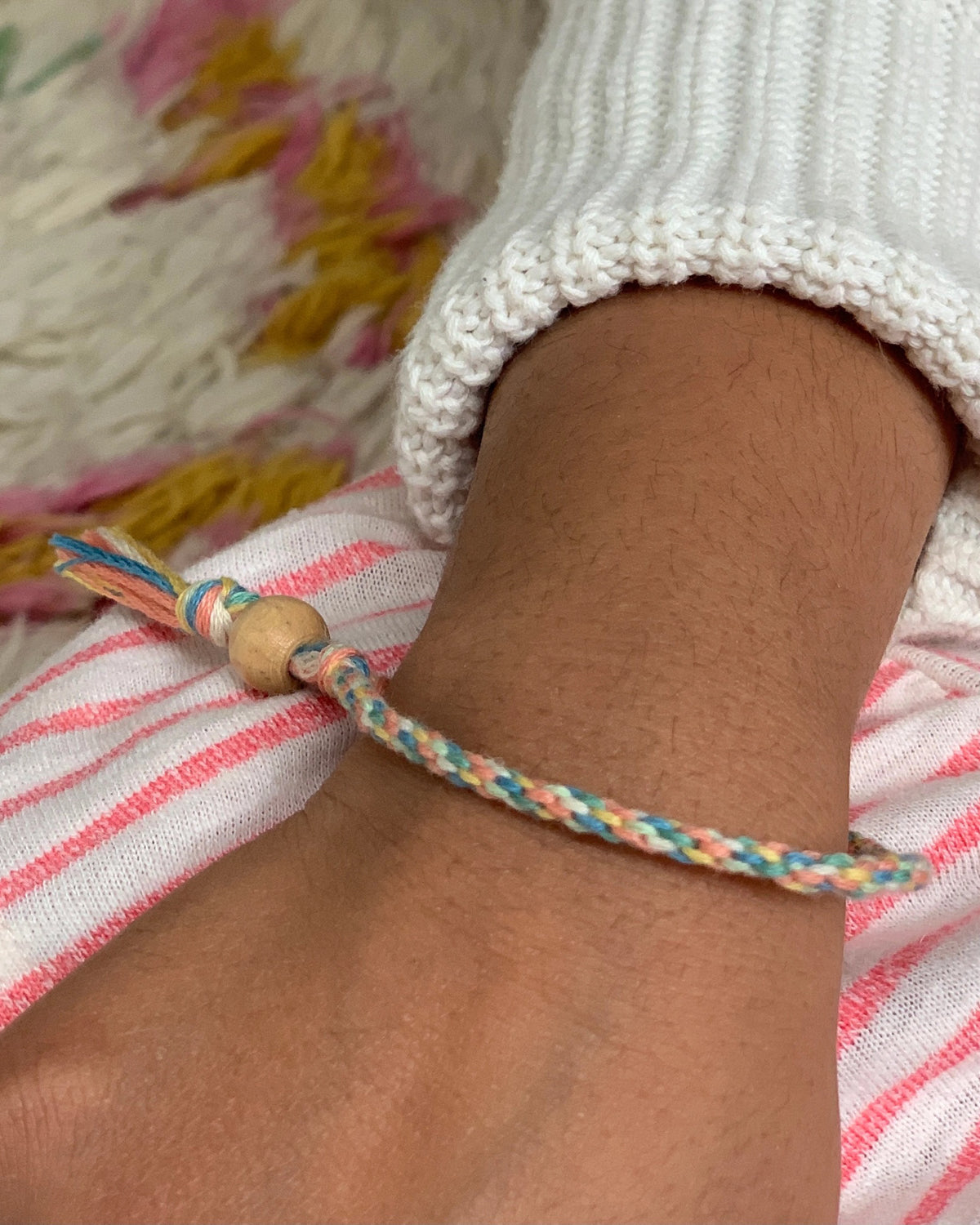 Wrist wearing a braided rainbow cotton friendship bracelet with a wooden bead