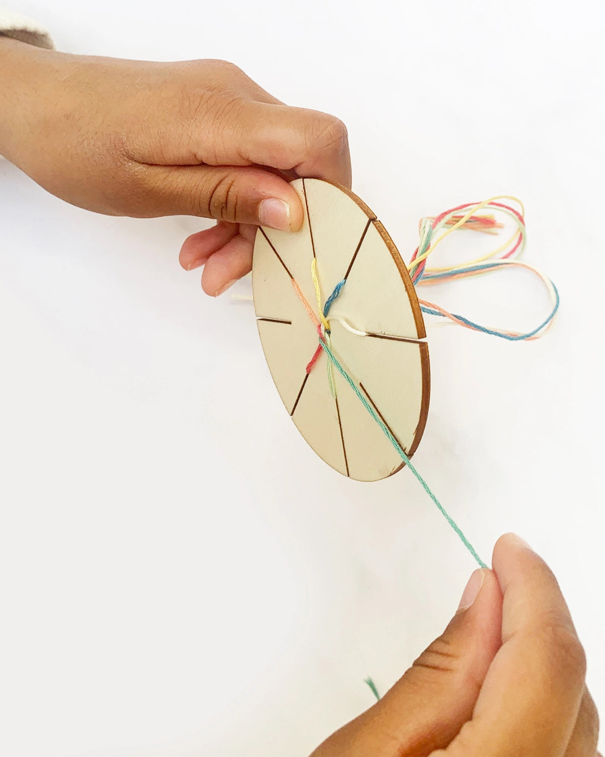 Hands braiding colorful thread on a wooden friendship bracelet disc