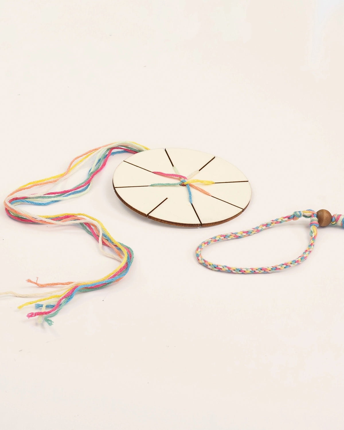 Wooden weaving disc threaded with colorful cotton beside a finished bracelet