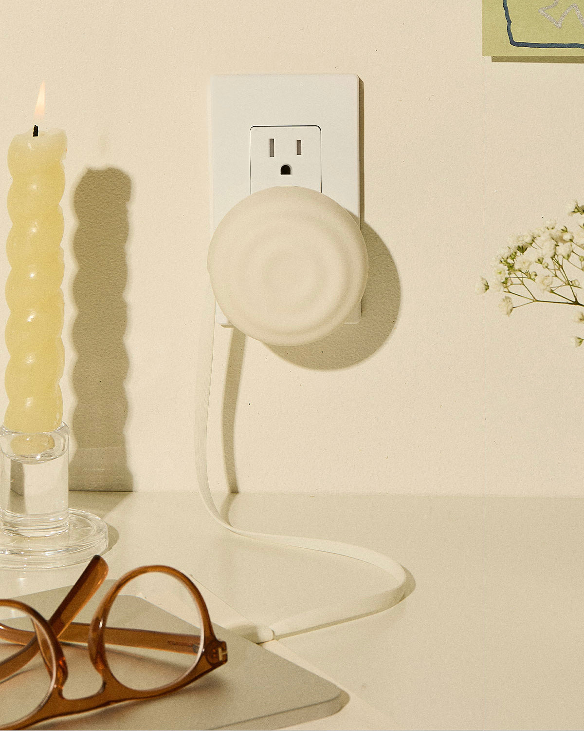 White Counterpart retractable USB-C charger plugged into a wall outlet beside a cream candle and tortoiseshell glasses