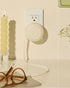 White Counterpart retractable USB-C charger plugged into a wall outlet beside a cream candle and tortoiseshell glasses