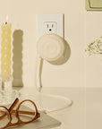 White Counterpart retractable USB-C charger plugged into a wall outlet beside a cream candle and tortoiseshell glasses