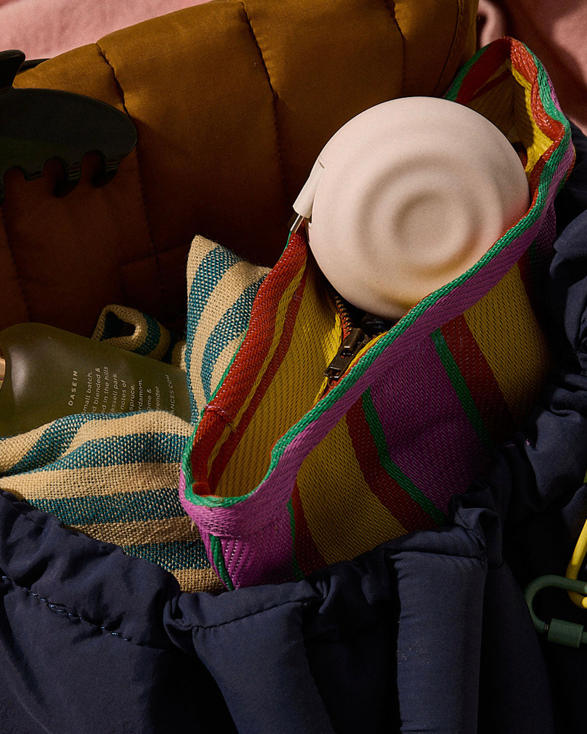 Round white USB-C charger tucked into a colorful striped woven tote next to a navy puffer jacket