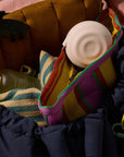 Round white USB-C charger tucked into a colorful striped woven tote next to a navy puffer jacket