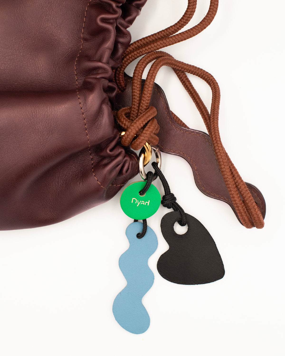 Close-up of Dyad chocolate brown leather bag with colorful deadstock-leather charms in blue and black.