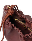 Close-up of a Dyad brown leather drawstring bag with gold zipper and hardware.