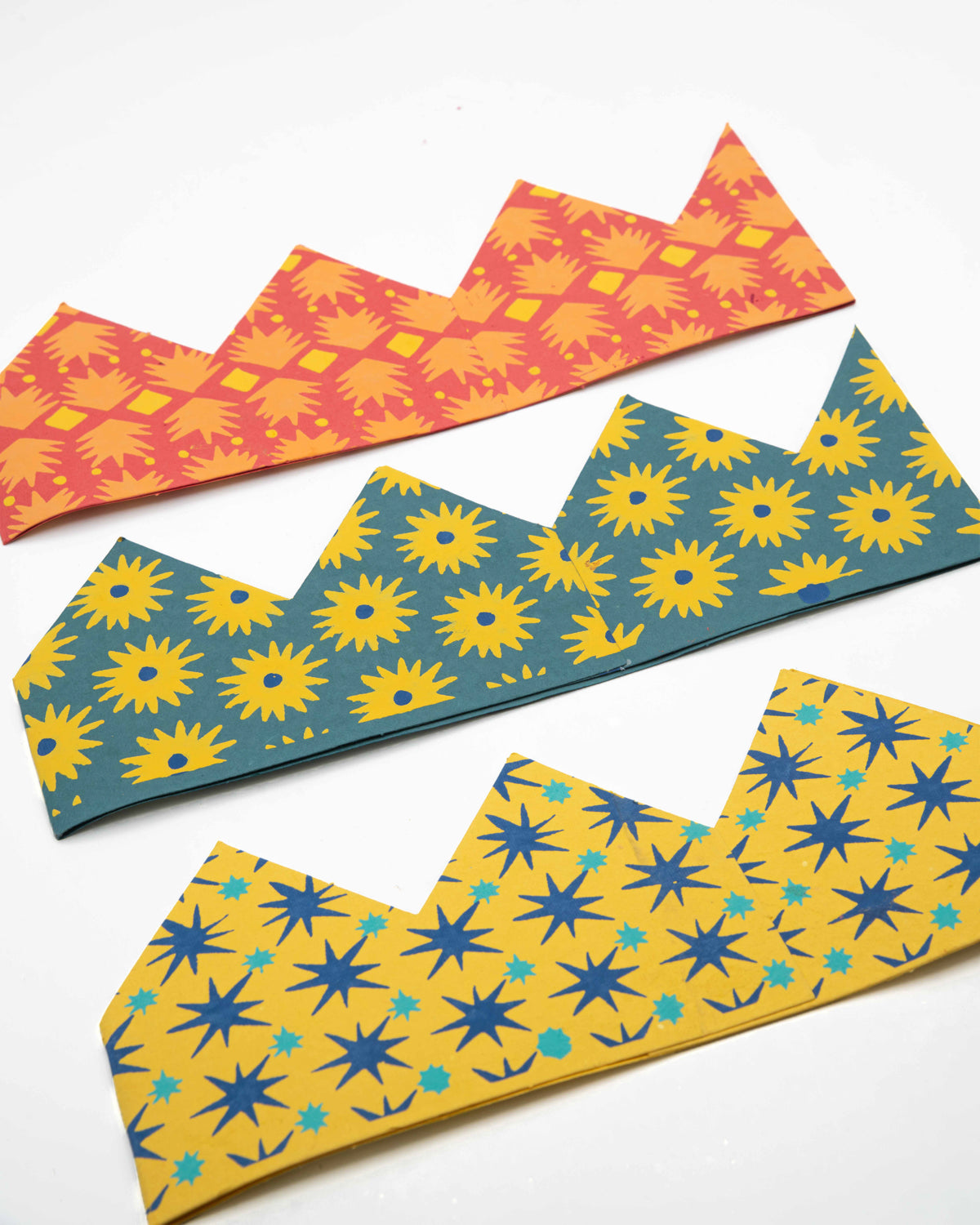 Three paper celebration crowns in orange, teal and mustard floral and star prints