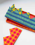 Blue and green striped paper crown on its orange gift box beside a red print crown
