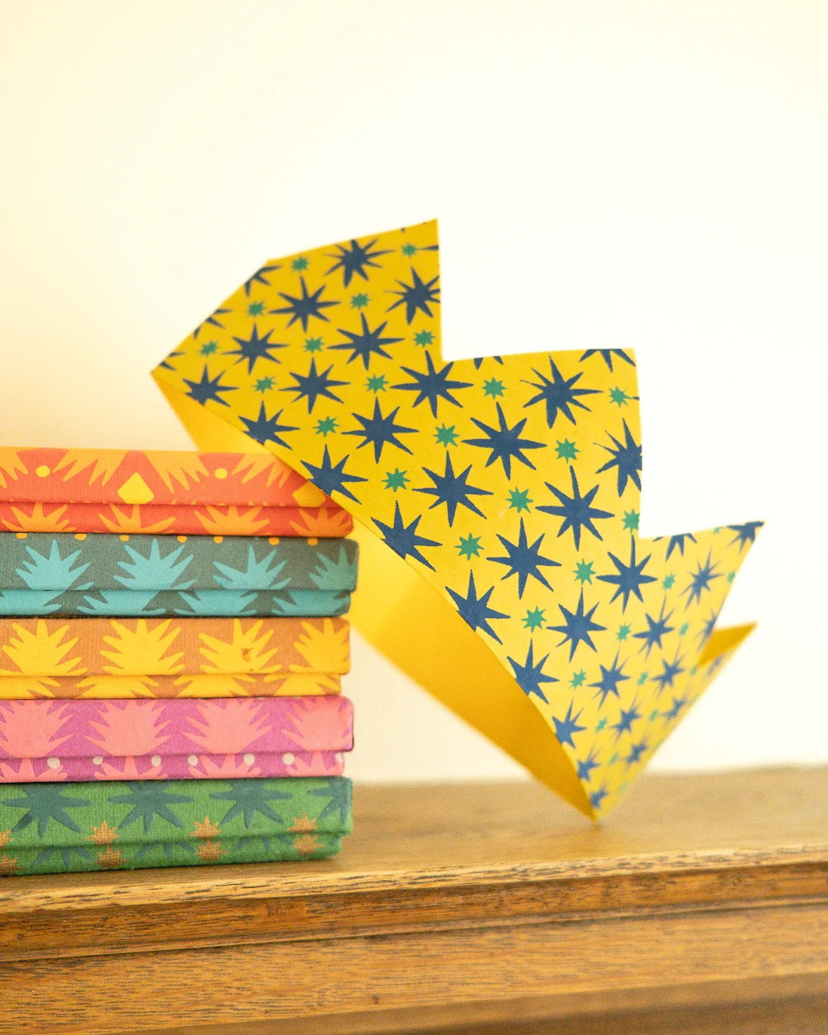 Mustard star-print paper crown standing in front of a stack of patterned crowns