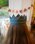 Child seen from behind wearing a navy and green paper crown in a festive room