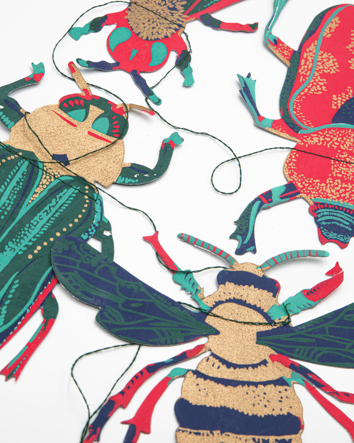 Close-up of hand screen-printed paper beetles and a bee in teal, red and metallic gold