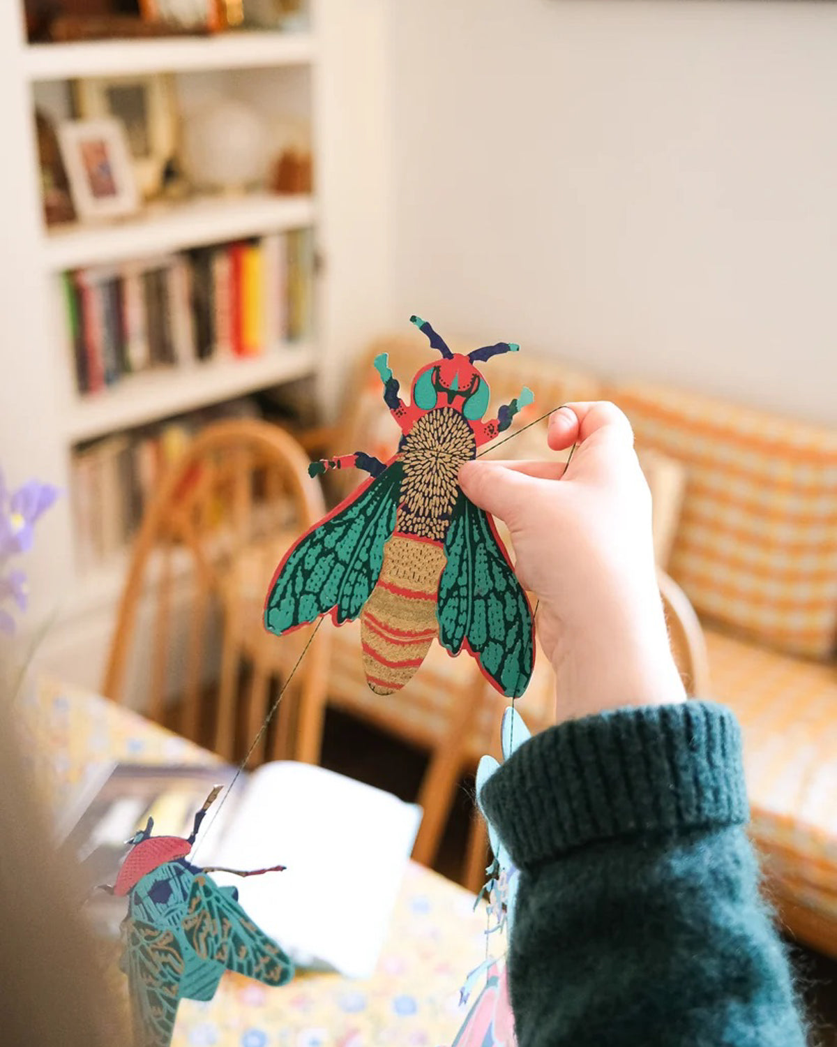 Child hanging a teal and gold paper moth from the insect garland in a sunny living room