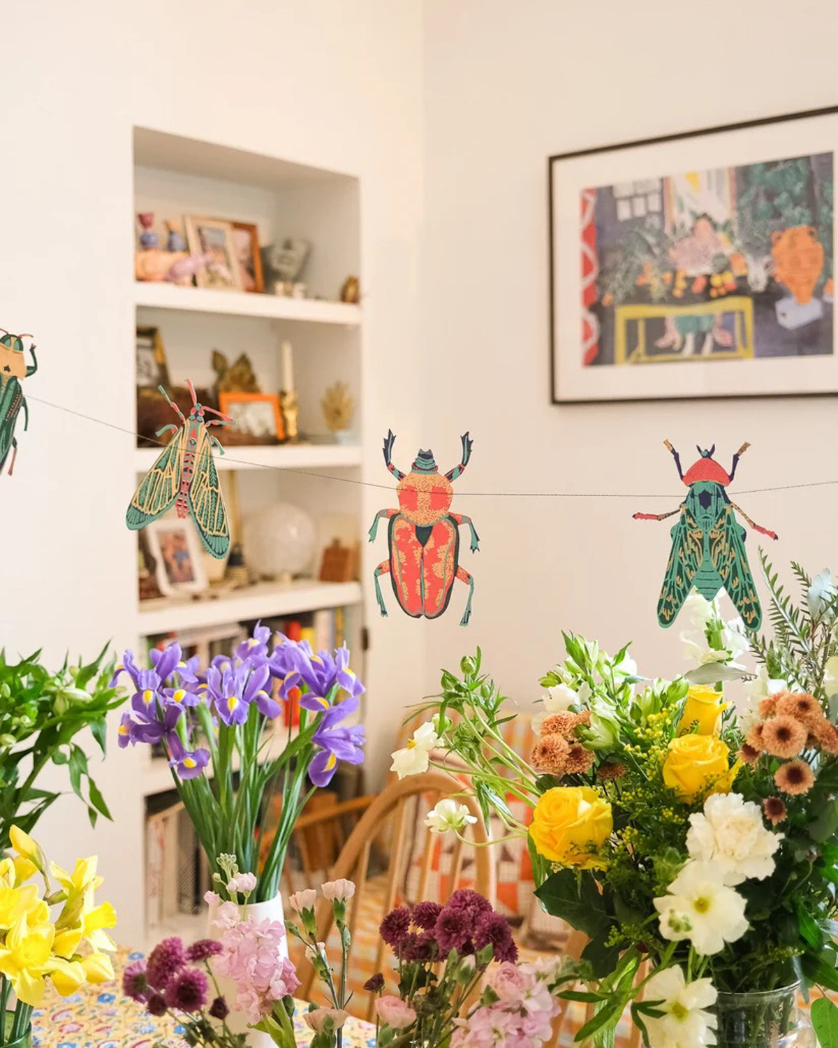 Insect paper garland strung across shelves above a table of spring flowers