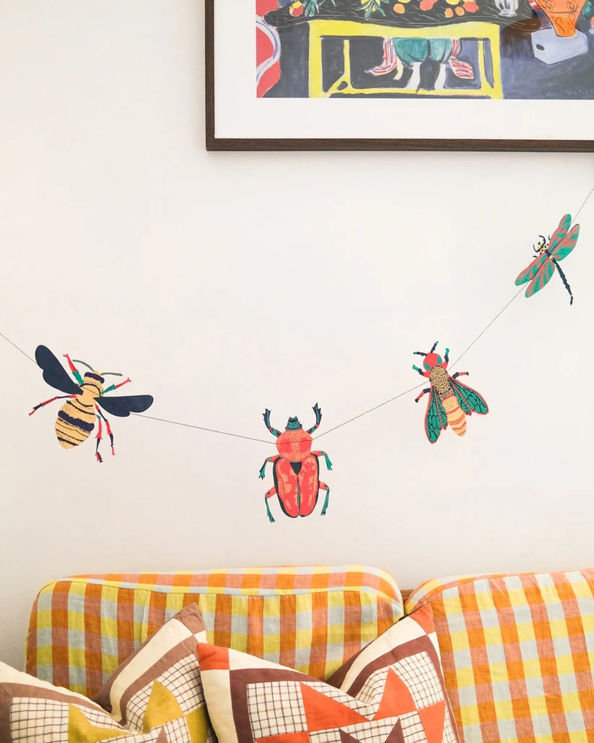 Insect paper garland with beetles, bees and a dragonfly strung above a checkered sofa