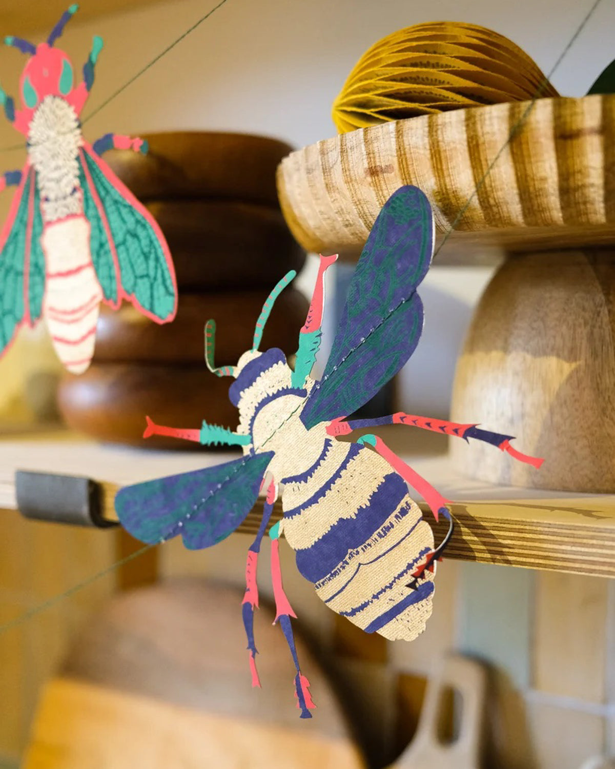 Screen-printed paper bee from the insect garland hanging beside wooden kitchen shelves