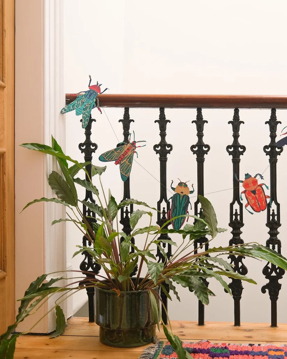 Paper insect garland draped along a black iron stair railing above a potted plant