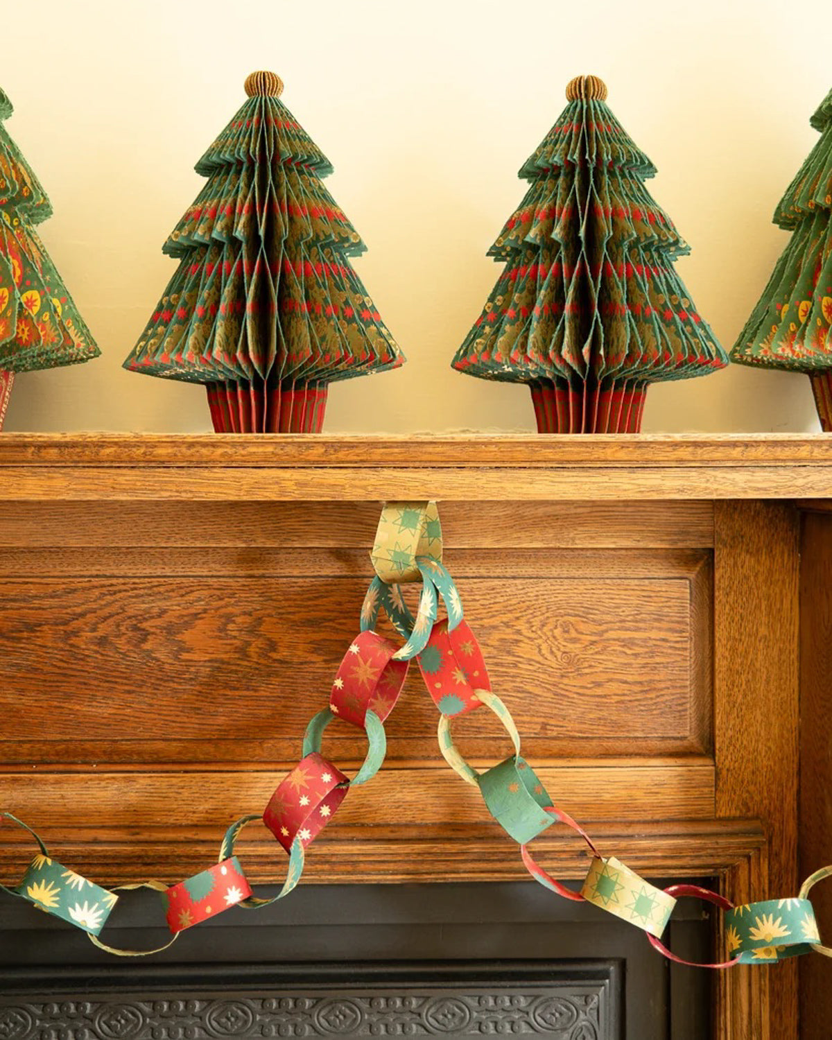 Red and green paper chains swagged across a fireplace mantel below paper Christmas trees