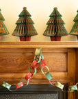 Red and green paper chains swagged across a fireplace mantel below paper Christmas trees