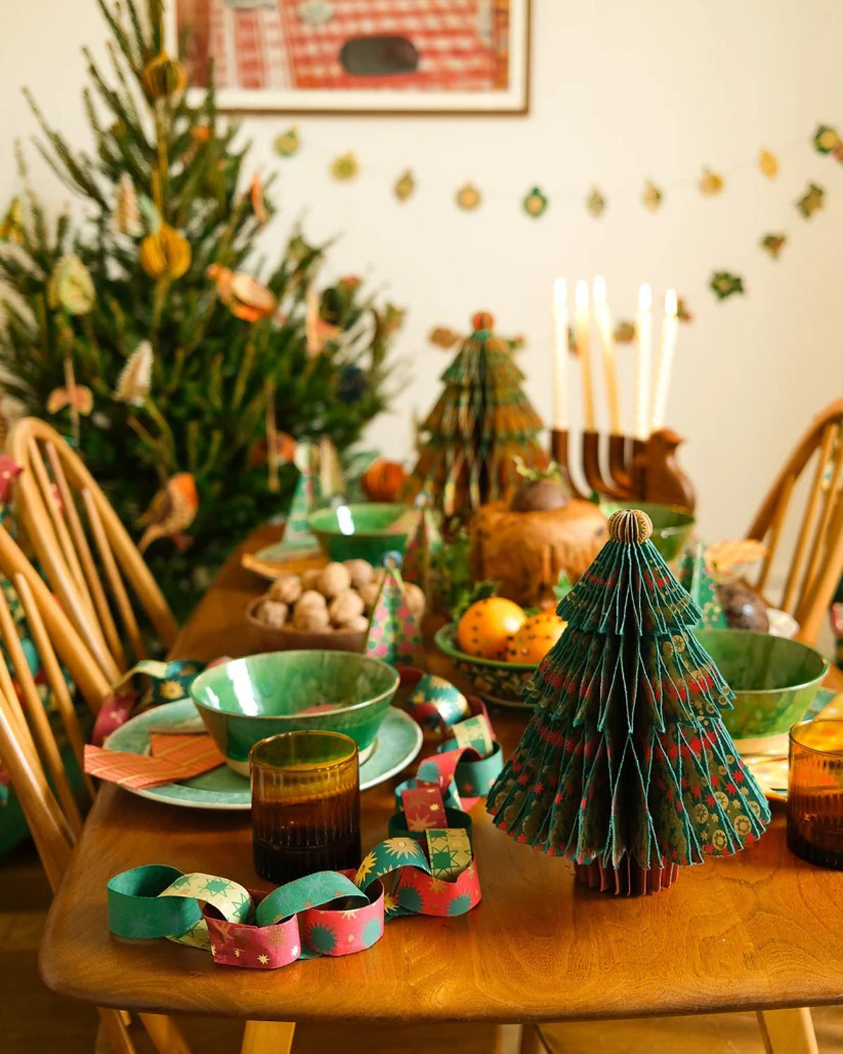 Paper chains strung along a holiday dinner table set with bowls, fruit and paper trees