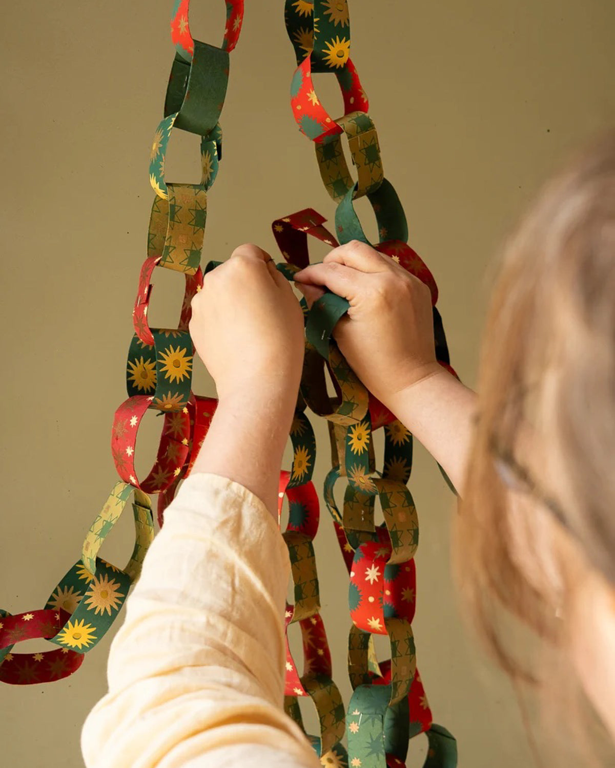 Hands linking hand-printed red and green paper chain strips