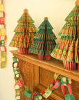 Patterned paper chains draped along a wooden mantel beside green paper Christmas trees