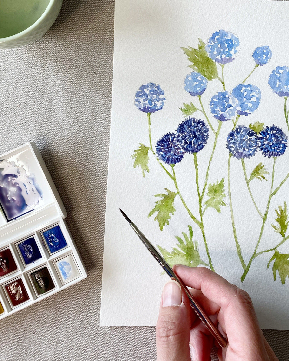 Hand painting blue wildflowers on a page of the watercoloring book