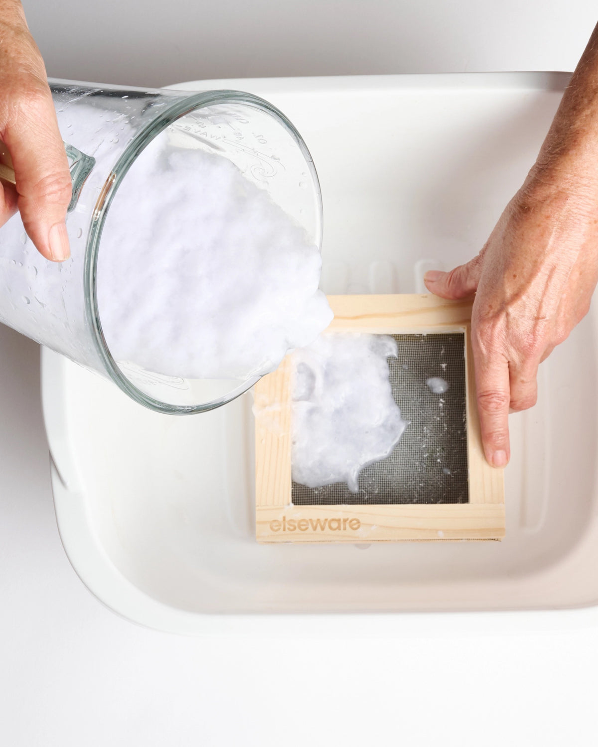 Hands pouring paper pulp into a wood mold set in a tub of water