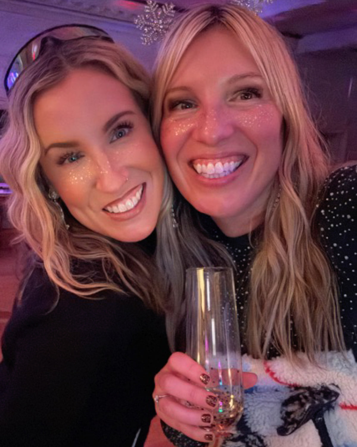 Two smiling women at a party wearing gold glitter freckles on their cheeks