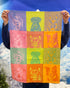 Person holding up a Garnier-Thiebaut Pop Art kitchen towel woven with rows of dog portraits in bright color blocks