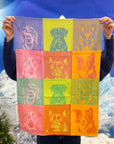 Person holding up a Garnier-Thiebaut Pop Art kitchen towel woven with rows of dog portraits in bright color blocks