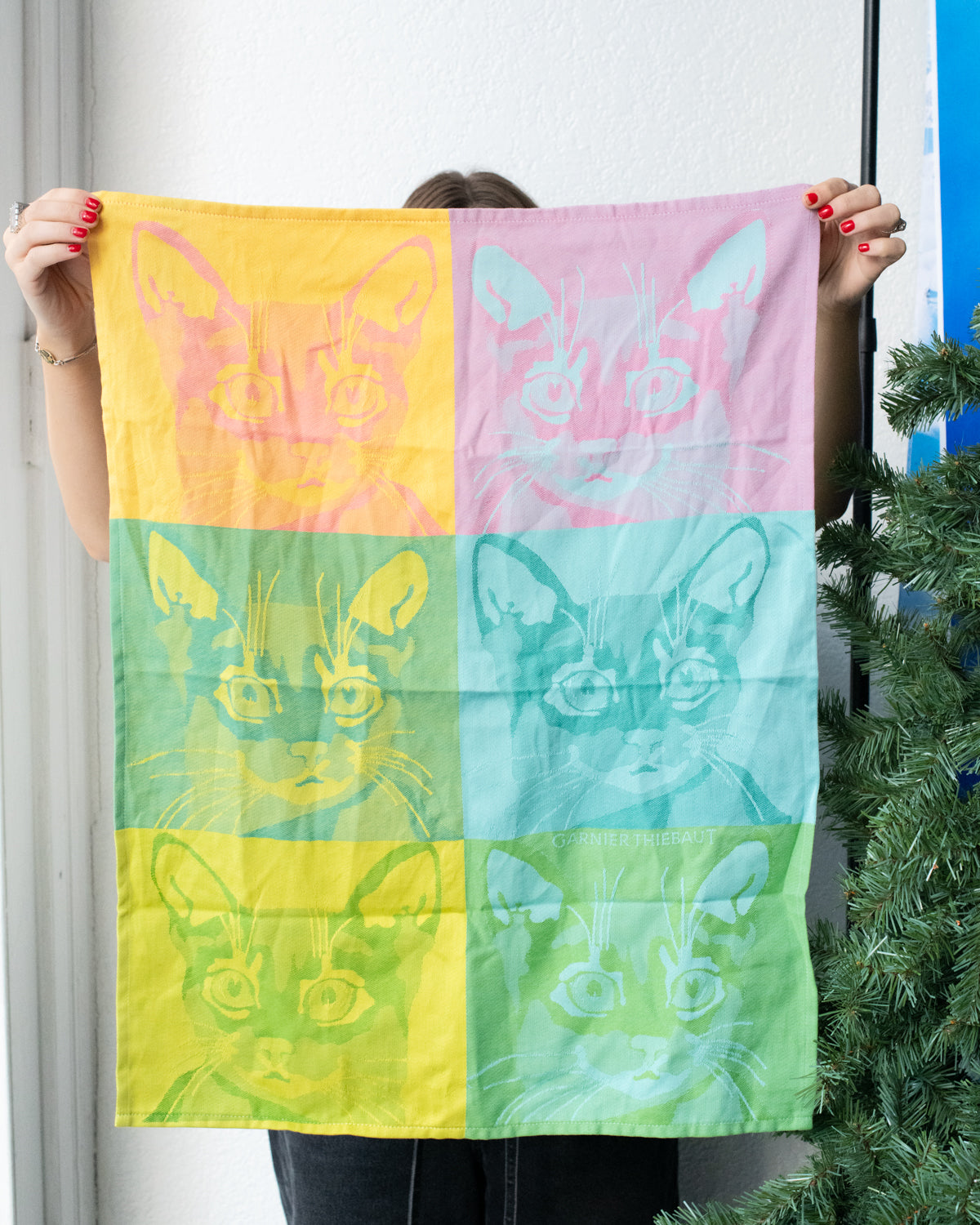 Person holding up the Chachacha pop art kitchen towel, with cat faces in yellow, pink, teal and green squares