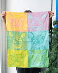 Person holding up the Chachacha pop art kitchen towel, with cat faces in yellow, pink, teal and green squares