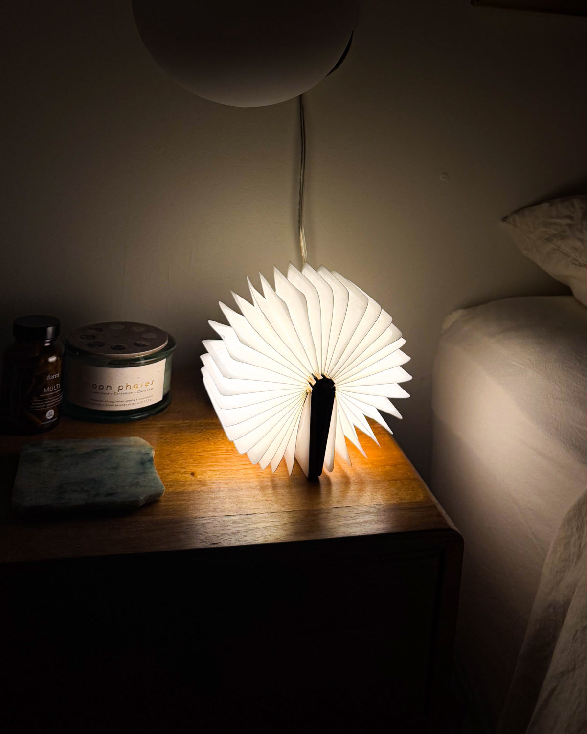 Gingko origami book light glowing open in a fan shape on a dark nightstand