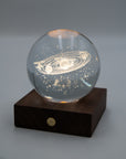Crystal ball with the solar system engraved inside, lit on a walnut base