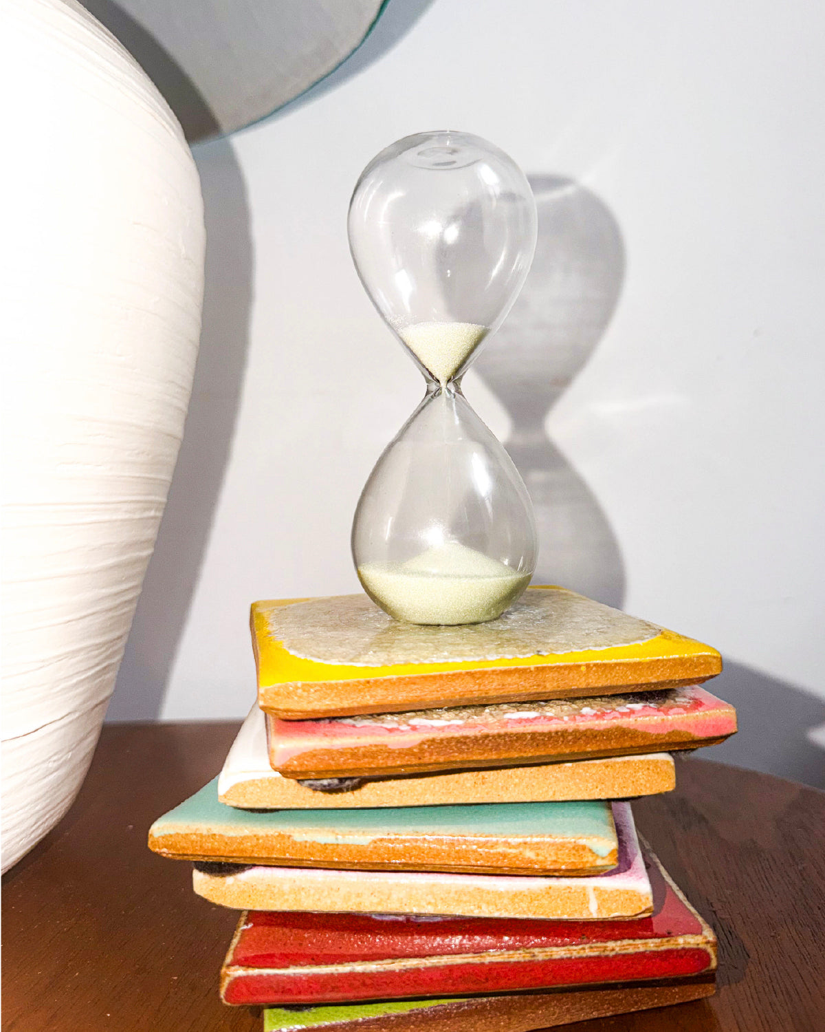 Gry Mattr 5-minute glass hourglass with pale sage sand on a stack of colorful tiles