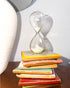 Gry Mattr 5-minute glass hourglass with pale sage sand on a stack of colorful tiles