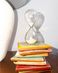 Gry Mattr 5-minute glass hourglass with pale sage sand on a stack of colorful tiles