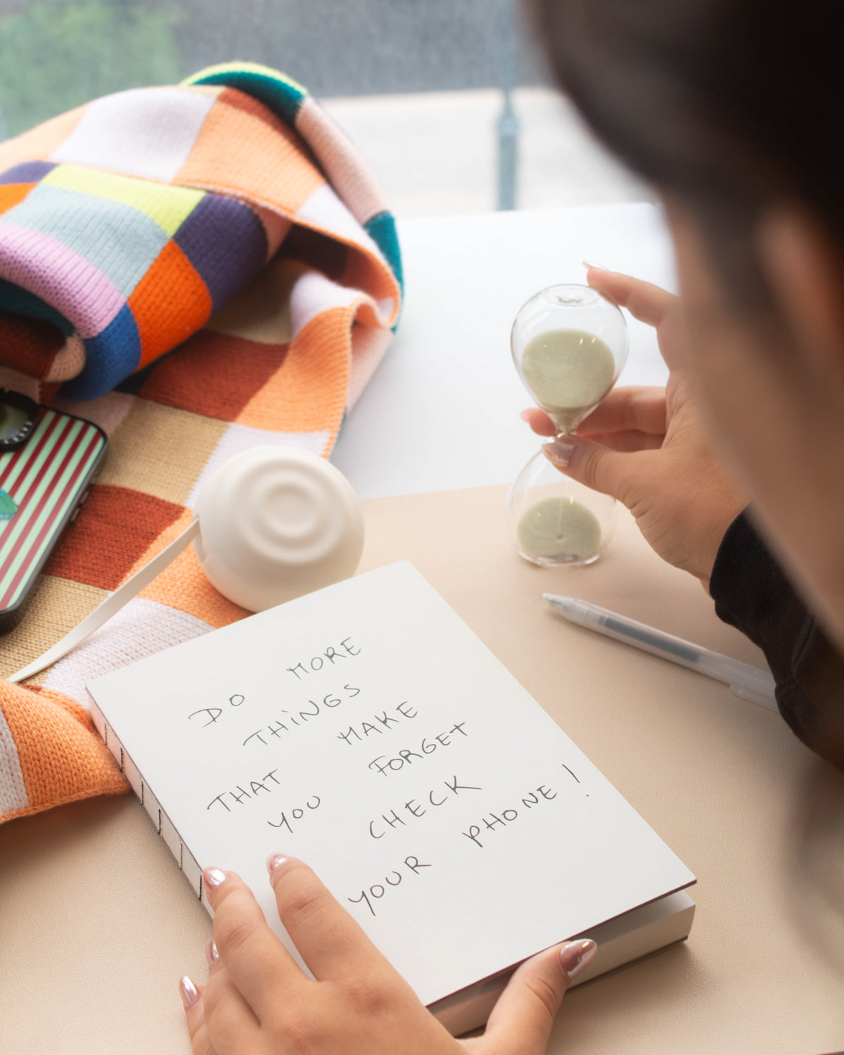 Person writing in a notebook next to a 5-minute sand timer on a desk