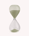 Glass desktop hourglass with pale sage green sand on a white background